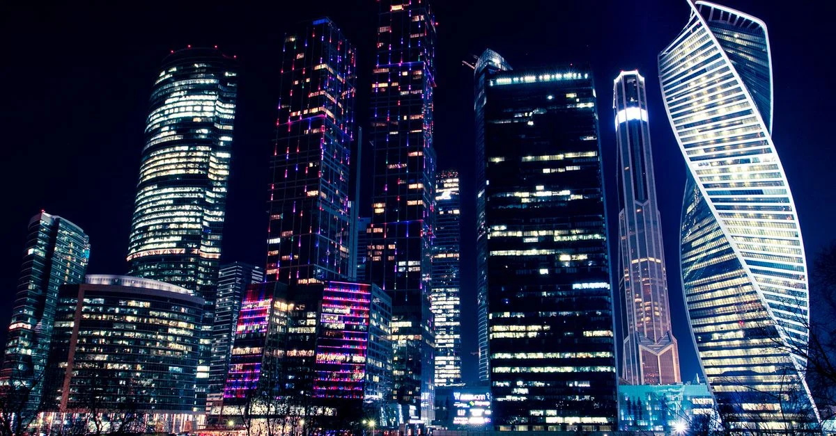 Vue nocturne illuminée des gratte-ciels modernes de Moscou, mettant en valeur les lumières vives de la ville et l'architecture urbaine.